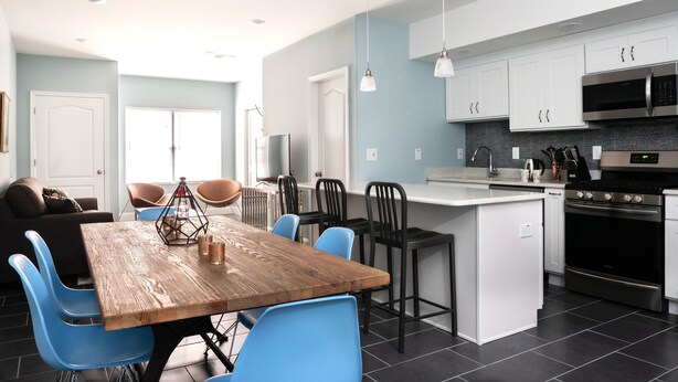 A modern kitchen with a wooden table, blue chairs, and stainless steel appliances. - 6 Bedroom Duplex Near NYC (Jersey City)