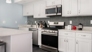 A modern kitchen with white cabinets, stainless steel appliances, and a tiled backsplash. - 6 Bedroom Duplex Near NYC (Jersey City)