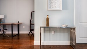 A room with a wooden floor, a glass table with a vase, a framed picture on the wall, and a white door. - 6 Bedroom Duplex Near NYC (Jersey City)