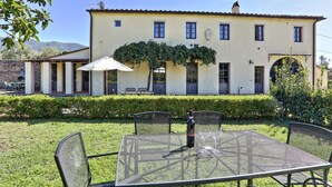 A building with a garden patio, outdoor seating, and a table with wine glasses. - Agriturismo Villa Rosselmini (Calci)