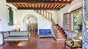 A spacious living area with a wooden staircase, a sofa, and a chair. - Agriturismo Villa Rosselmini (Calci)