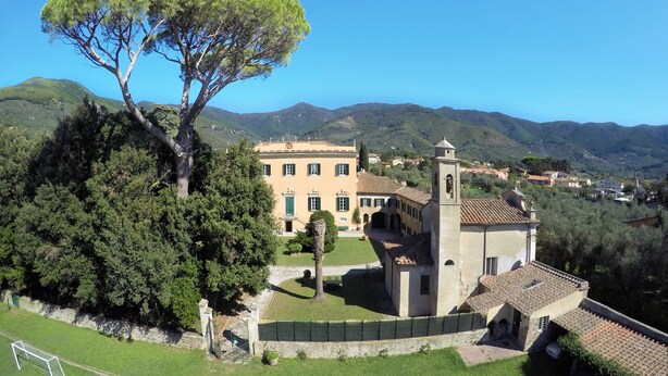 A large building with a tower, surrounded by lush greenery and hills in the background. - Agriturismo Villa Rosselmini (Calci)
