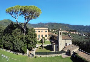 A large building with a tower, surrounded by lush greenery and hills in the background. - Agriturismo Villa Rosselmini (Calci)