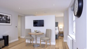Un salon moderne avec une table ronde, deux fauteuils, un téléviseur fixé au mur, une horloge et un radiateur.