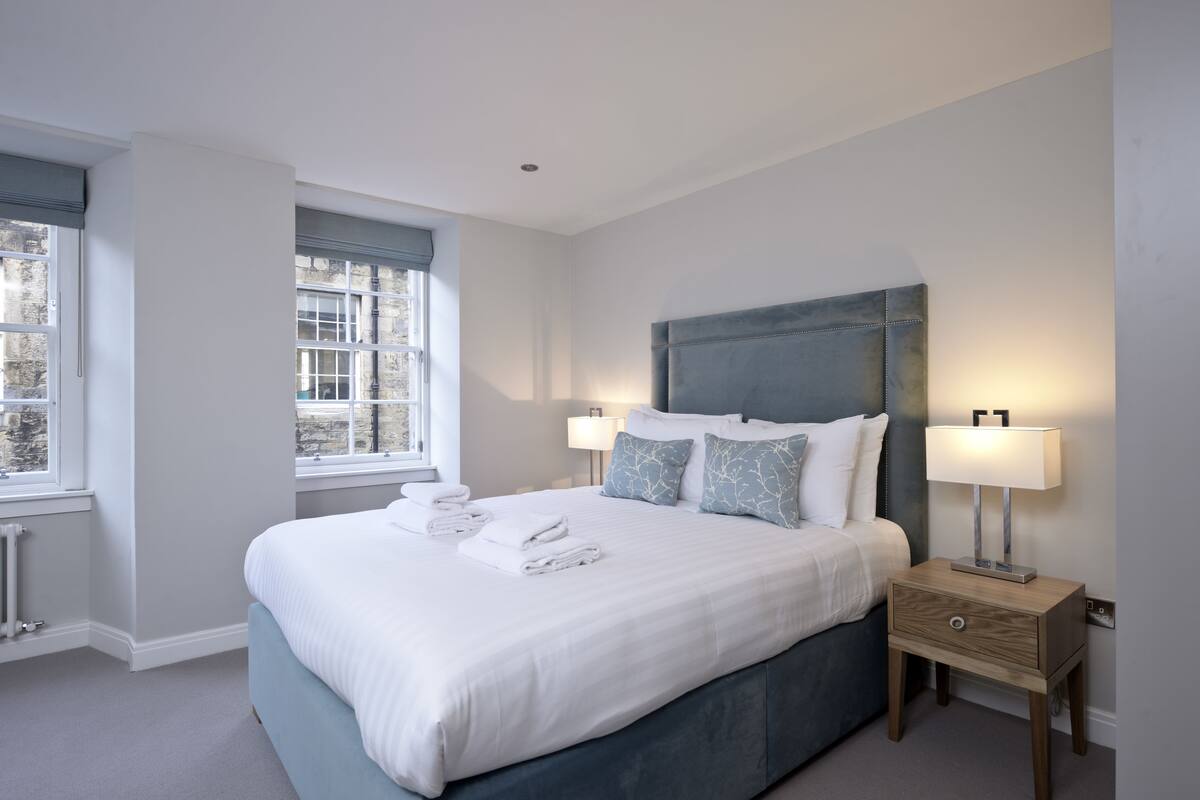 A modern bedroom with a large bed, two bedside tables with lamps, and a window with blinds.