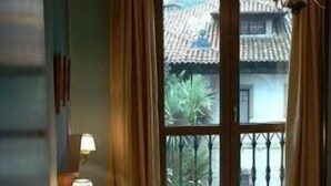 Una habitación de hotel con una cama, una mesita de noche con lámpara y una ventana con cortinas.