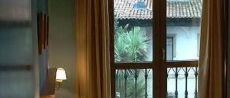 A hotel room with a bed, a nightstand with a lamp, and a window with curtains.