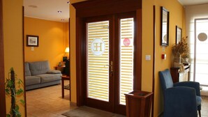 Un vestíbulo de hotel con un mostrador de recepción, un sofá, un sillón azul y una puerta de madera con un cartel.