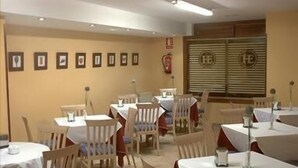 Comedor con varias mesas y sillas, un extintor en la pared y una ventana con persianas.