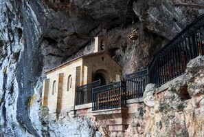 A small building with a bell tower, built into a rocky cliffside. - La Estrada (Parres)