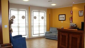 Un área de recepción con un escritorio de madera, un sillón azul, un sofá gris y un amplio ventanal con vistas.