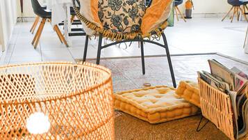 Une pièce comprenant une table à manger, des chaises, un fauteuil en osier, un tapis tissé et un porte-revues.