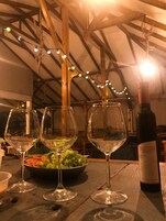 Una mesa con tres copas de vino y una botella, un bol de ensalada y luces cálidas en un ambiente rústico.