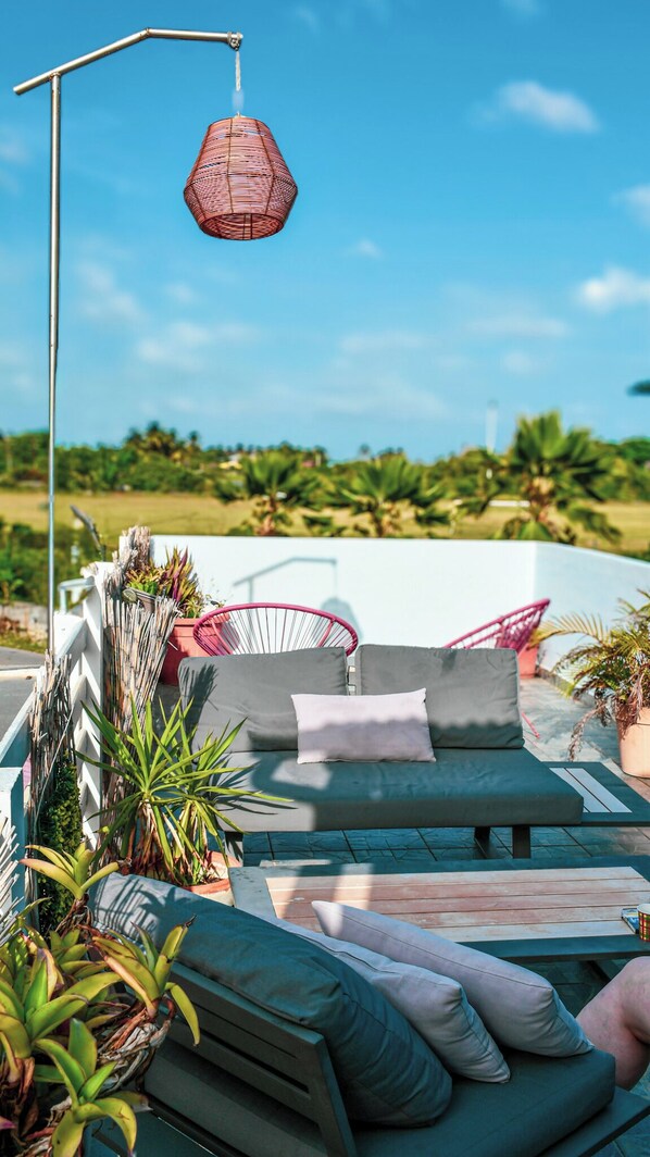 An outdoor seating area with a sofa, cushions, and a hanging light fixture. - Hotel OASIS (La Desirade)