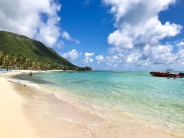 Una playa con agua turquesa cristalina, una orilla arenosa y un bote rojo anclado cerca de la costa.