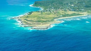 An aerial view of a coastal island with a small settlement, clear blue waters, and a hilly landscape.