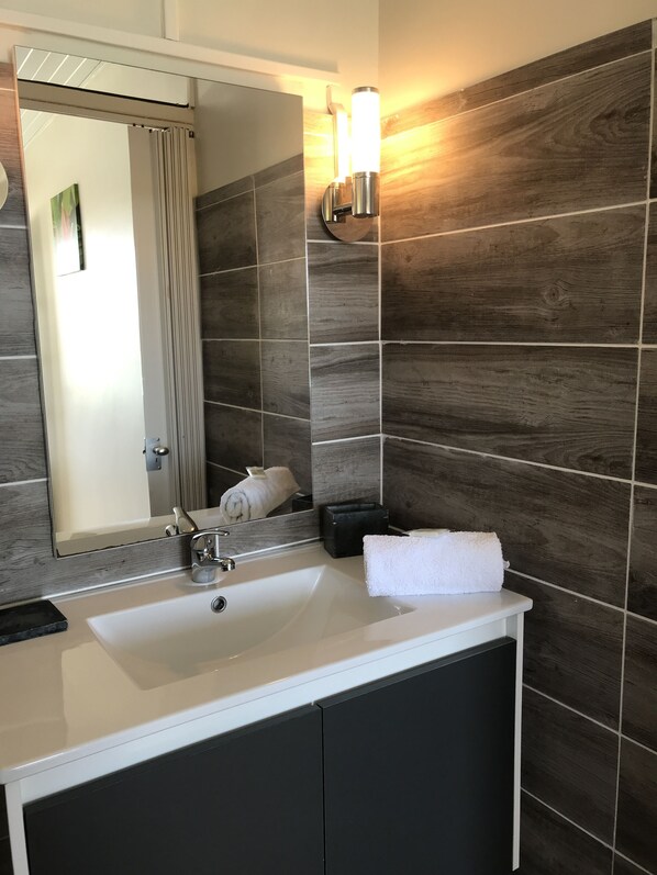 Un baño con un lavabo blanco, baldosas oscuras, un espejo y una toalla.
