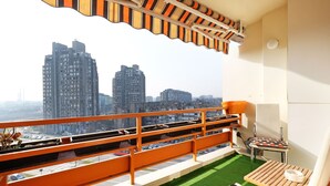 A balcony with a view of tall buildings, a small table with a chair, and a green artificial grass area. - Apartment Bella Art (Belgrade)
