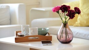 A white table with a tray holding two white mugs, a green bowl, and a smartphone. A pink vase with flowers is also on the table. - Apartment Bella Art (Belgrade)