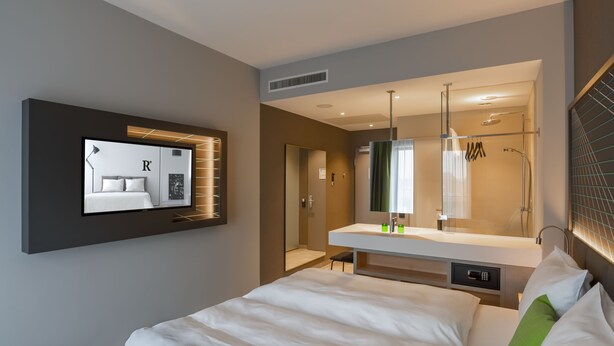 A modern hotel room with a large bed, a built-in TV, a bathroom with a glass shower enclosure, and a vanity with a mirror. - elaya hotel kevelaer, Trademark Collection by Wyndham (Kevelaer)