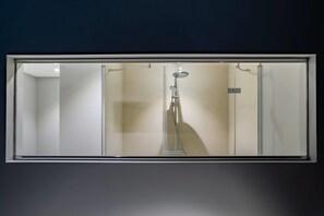 Un bany amb una cabina de dutxa de vidre, un vàter manual i un robinet fixat a la paret.