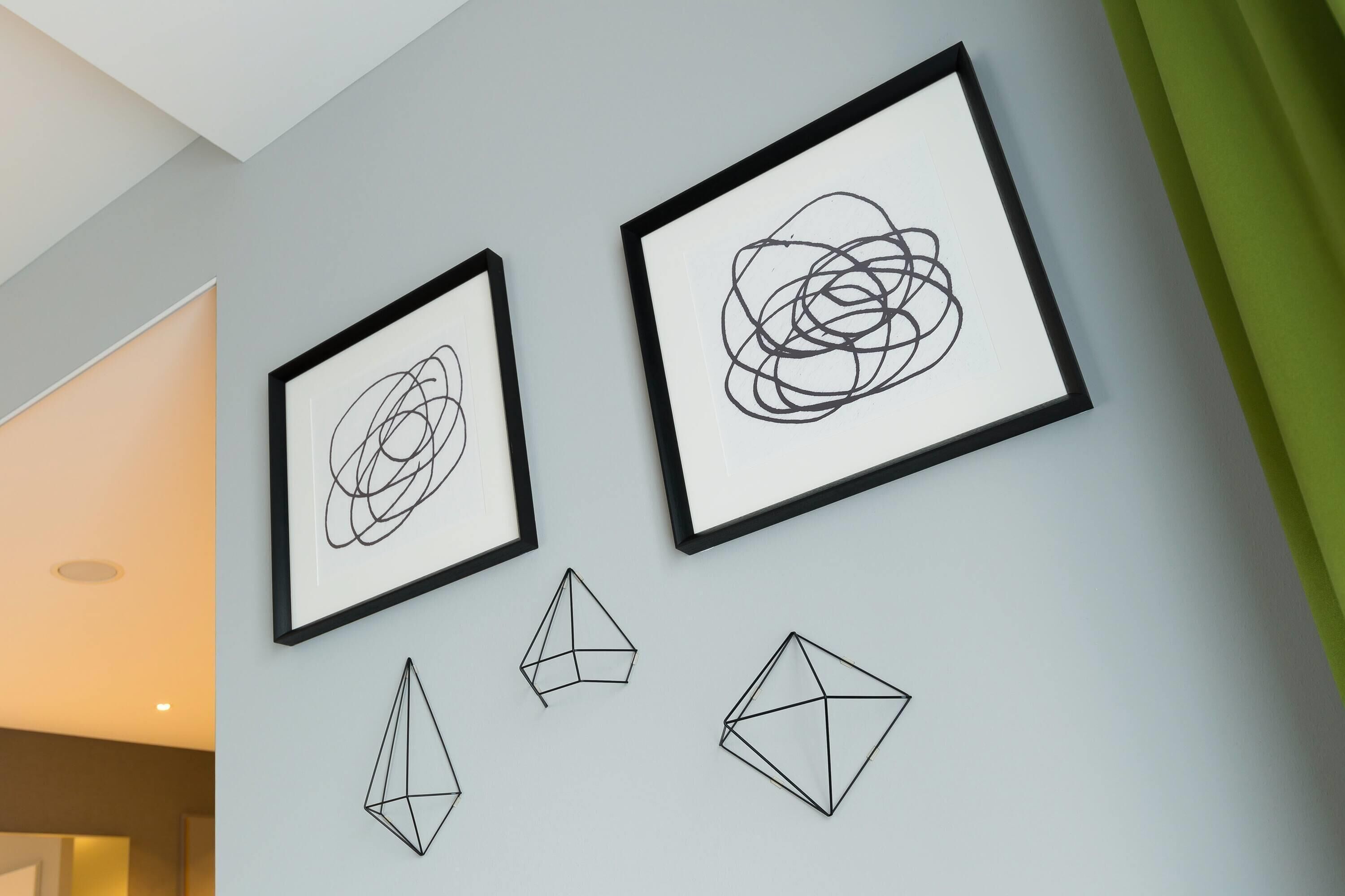 A wall with three framed artworks and two geometric sculptures.