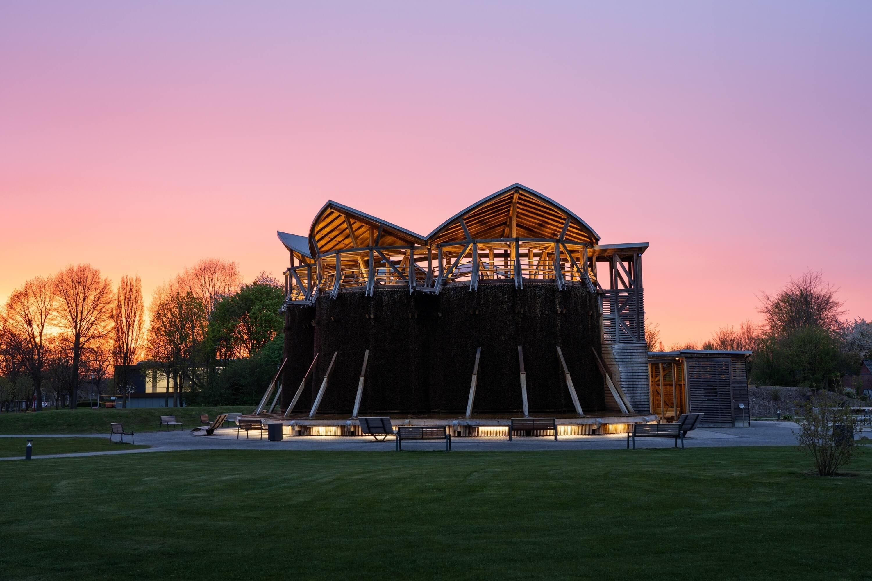 A modern building with a unique roof structure, surrounded by a grassy area and trees.