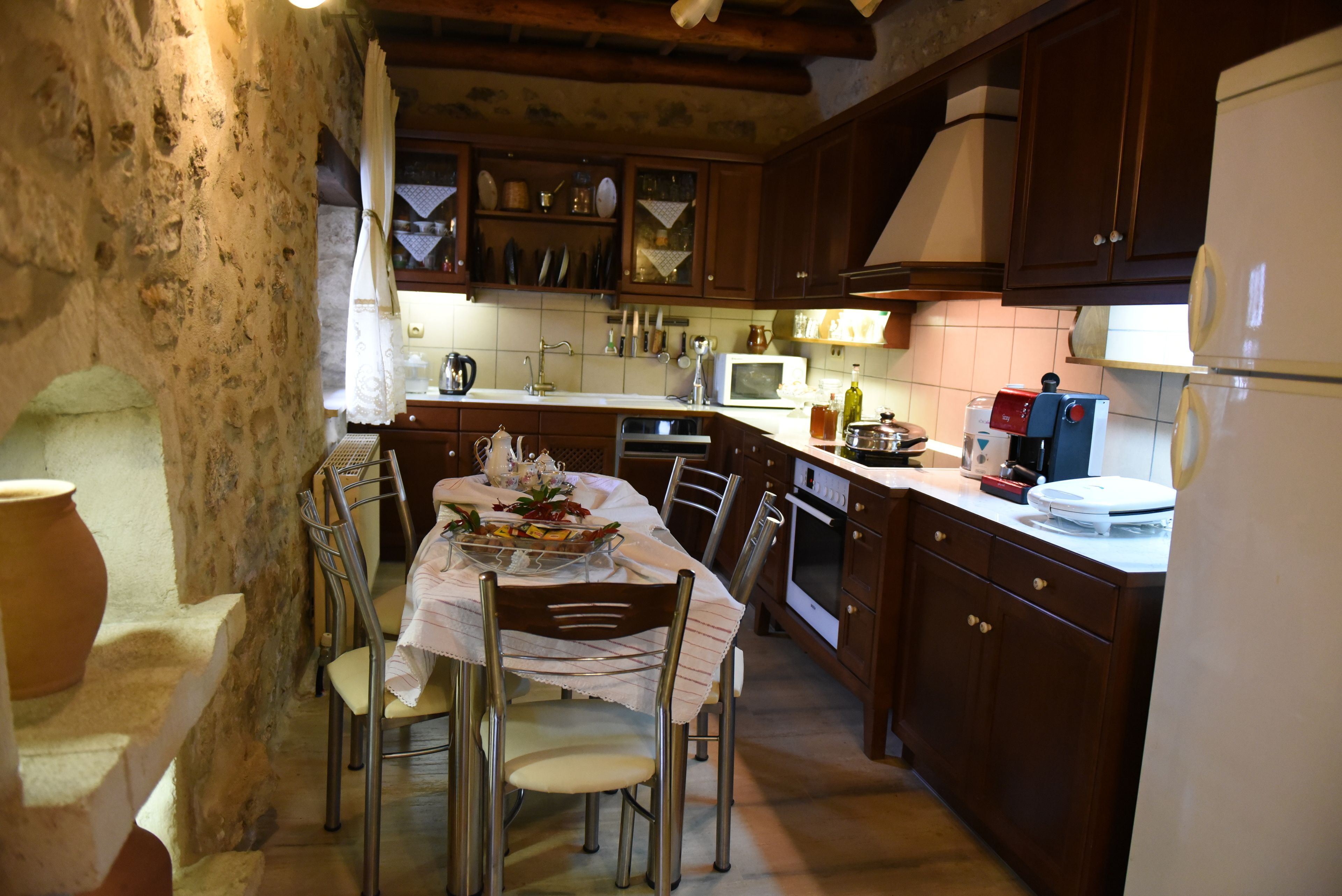 Uma cozinha rústica com armários de madeira, uma mesa de jantar posta para quatro pessoas e uma parede de pedra.