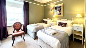 Ein Hotelzimmer mit zwei Betten, einem Sessel, einem Fenster mit Vorhängen, einem Zebra-Gemälde und Nachttischlampen.