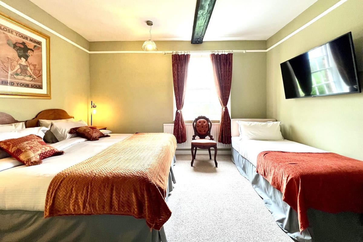 A hotel room with two beds, a chair, a television, and a poster on the wall.