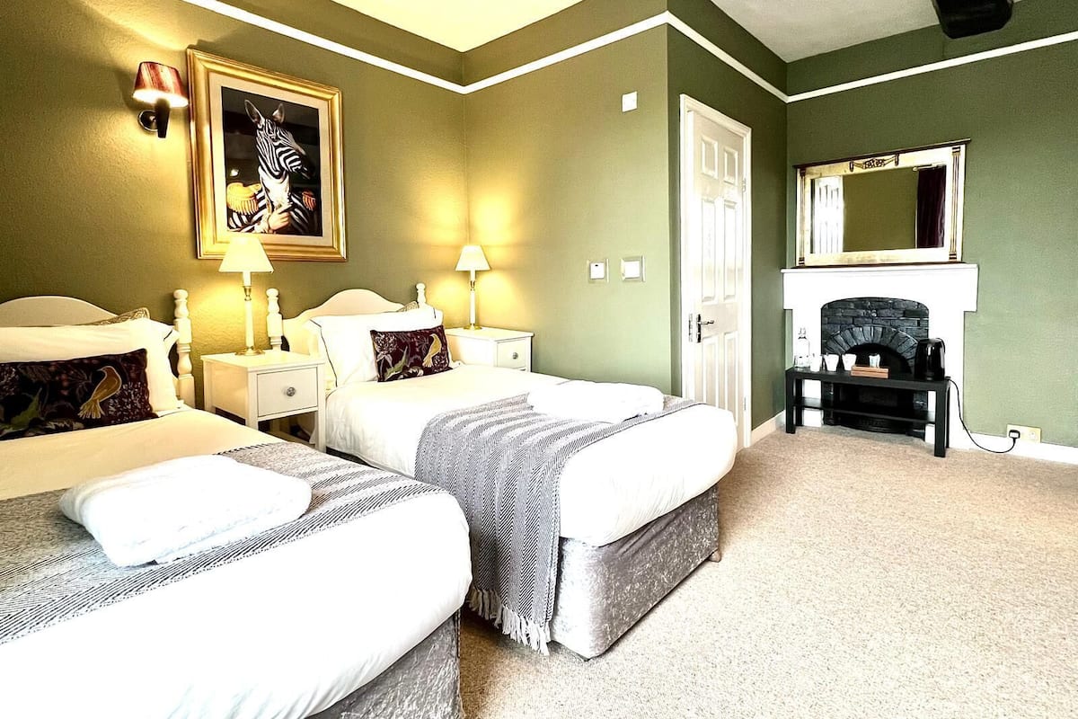 A hotel room with two beds, a fireplace, a mirror, and a framed picture on the wall.