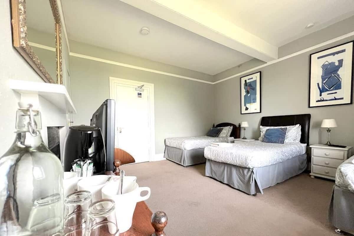 A hotel room with two beds, a desk, a chair, a mirror, and a door.