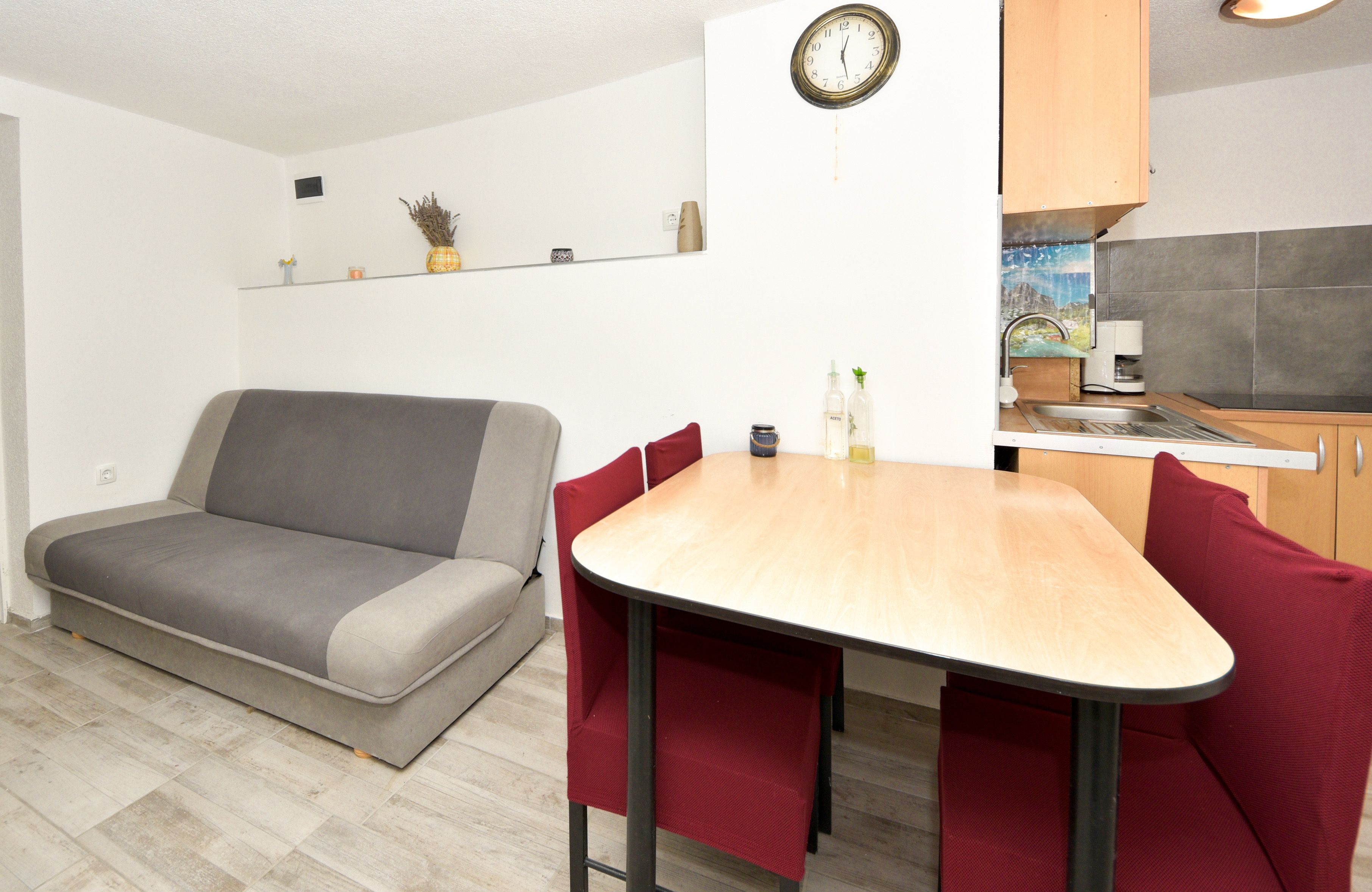 A compact living space with a sofa, a dining table with chairs, a kitchen area, and a wall clock.