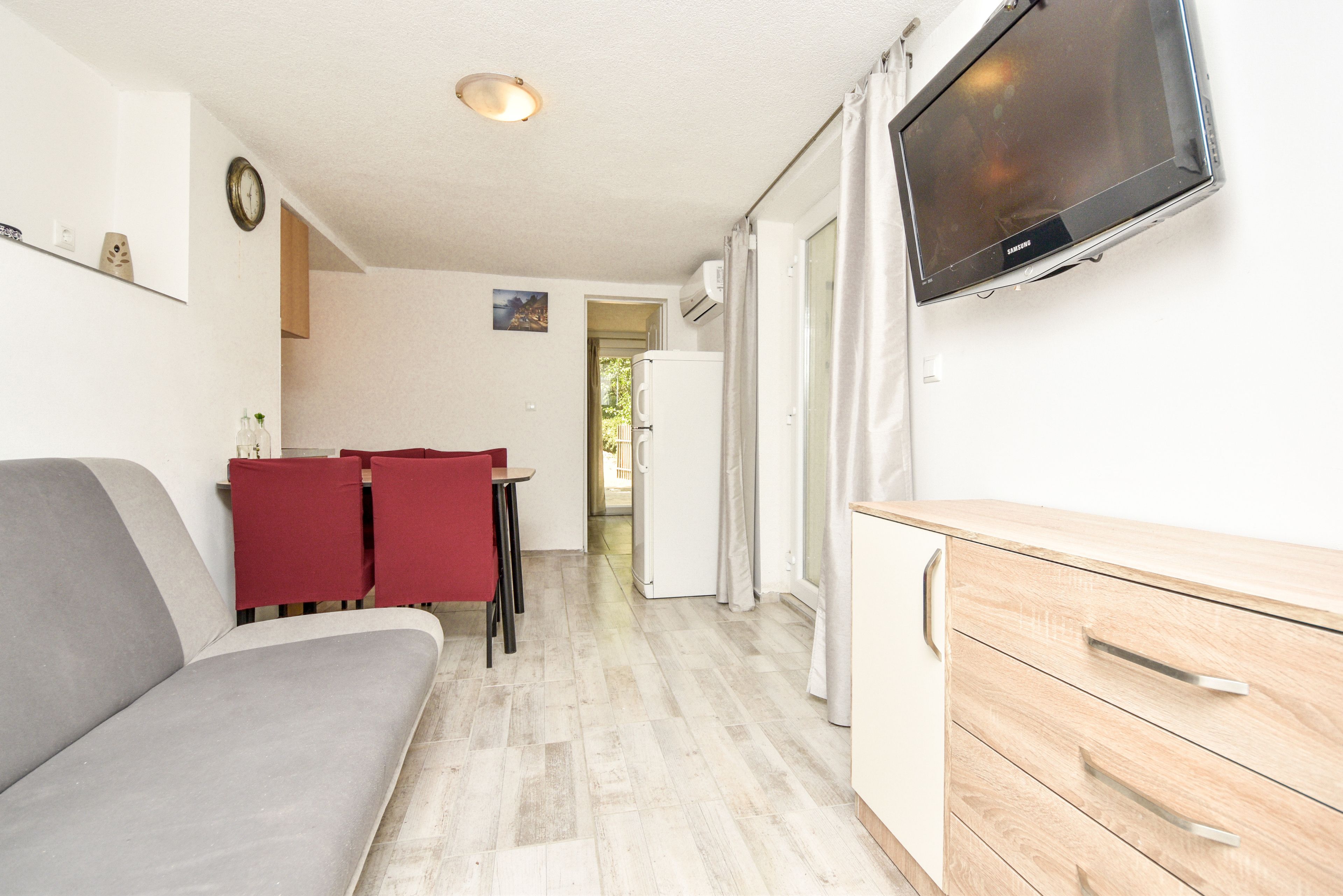 A compact room with a sofa, a small table with chairs, a wooden cabinet, and a television mounted on the wall.