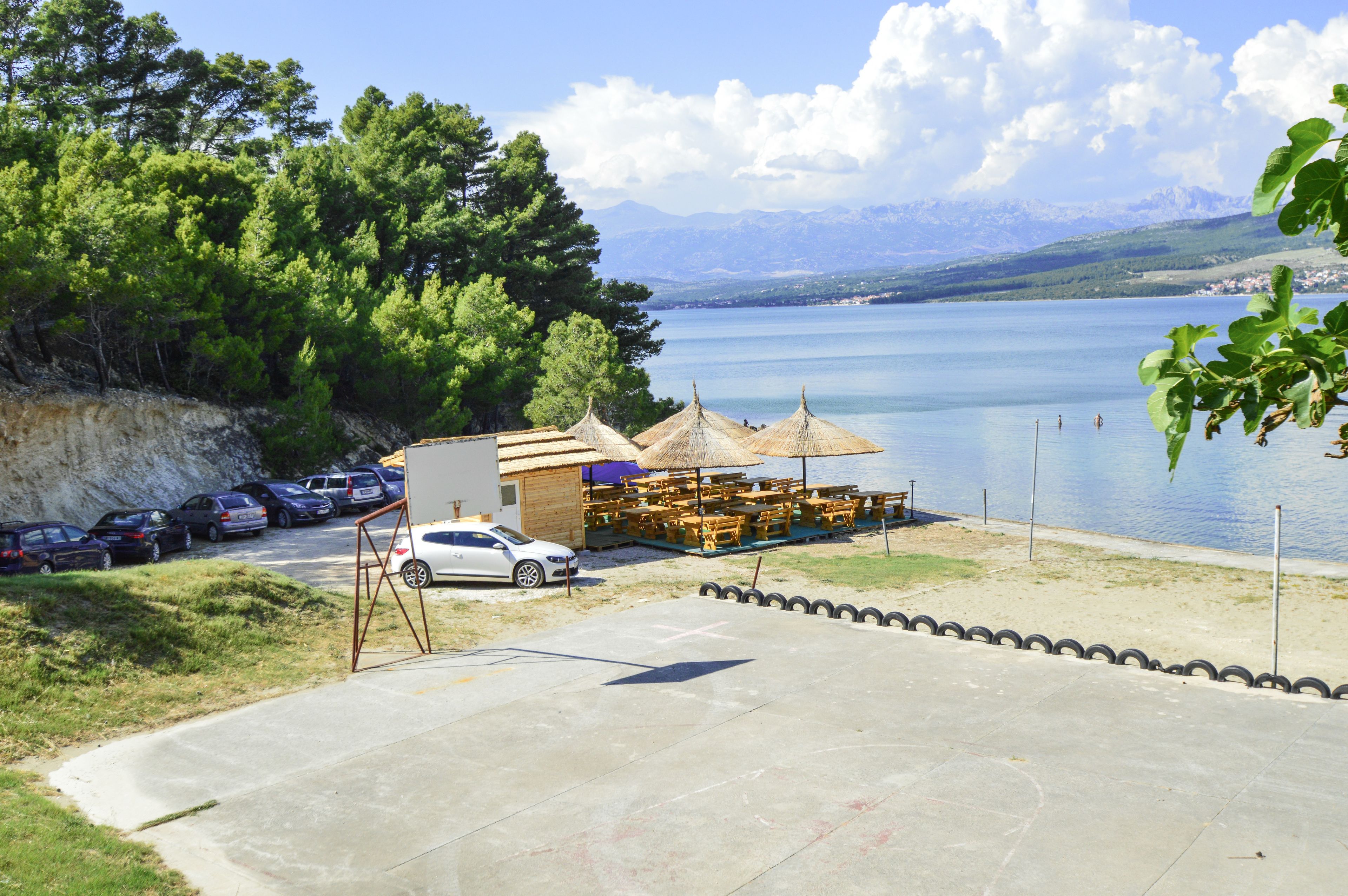 A lakeside area with a small building, outdoor seating, and parked cars.