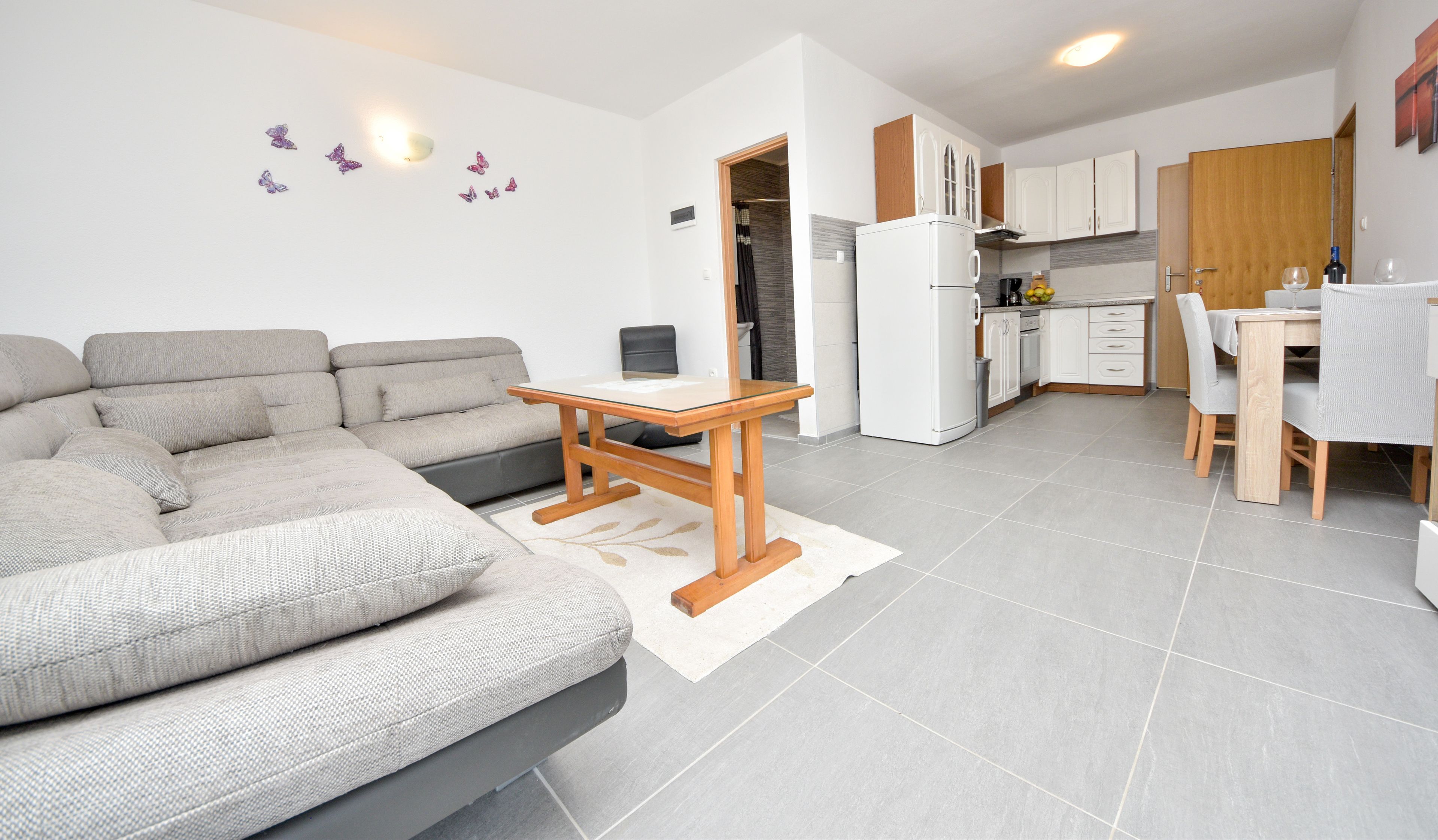 A modern apartment with a grey sofa, a wooden coffee table, a kitchen with white cabinets, and a dining area.