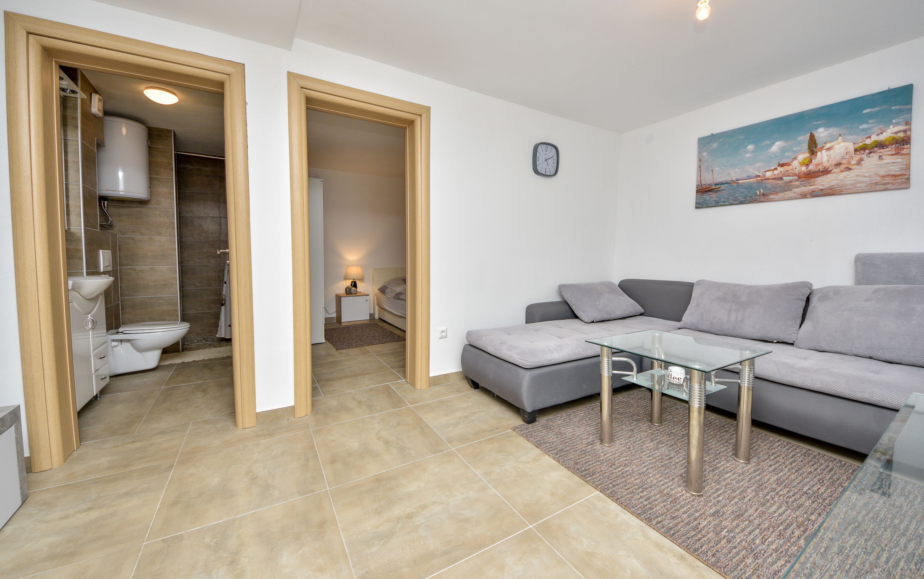 A modern living room with a grey sofa, a glass coffee table, and a painting on the wall.