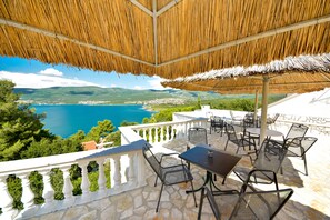 An outdoor patio with a thatched roof, stone flooring, and metal chairs and tables. - Apartmani Robi i Kristina (Benkovac)