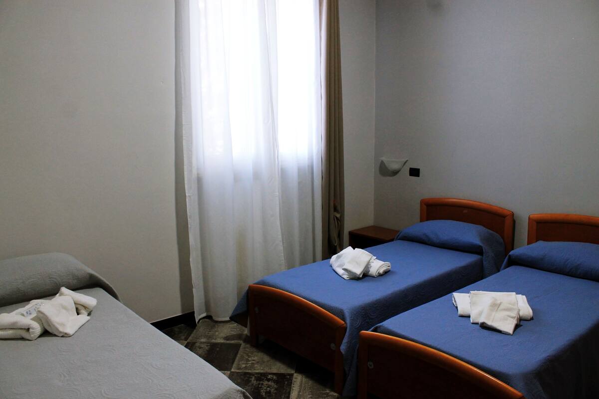 A hotel room with two single beds, a small table, and a window with curtains.