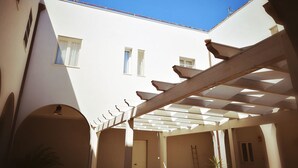 A covered outdoor area with a white building in the background, a wooden pergola, and a ladder. - il Chiostro delle Cererie (Matera)