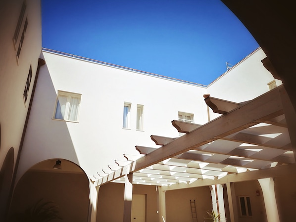 A covered outdoor area with a white building in the background, a wooden pergola, and a ladder. - il Chiostro delle Cererie (Matera)