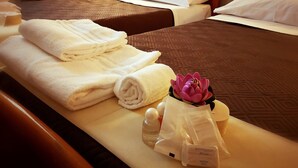A hotel room with two beds, each with a brown quilted bedspread, white pillows, and neatly folded white towels on the side. A decorative purple flower and a bottle of soap are also visible on the bed. - il Chiostro delle Cererie (Matera)