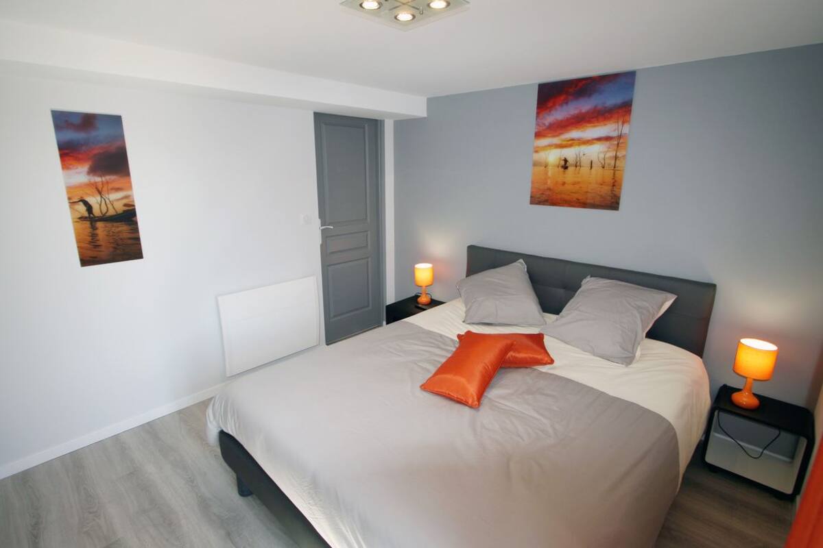Une chambre moderne avec un grand lit, deux tables de chevet, une porte et deux tableaux accrochés au mur.