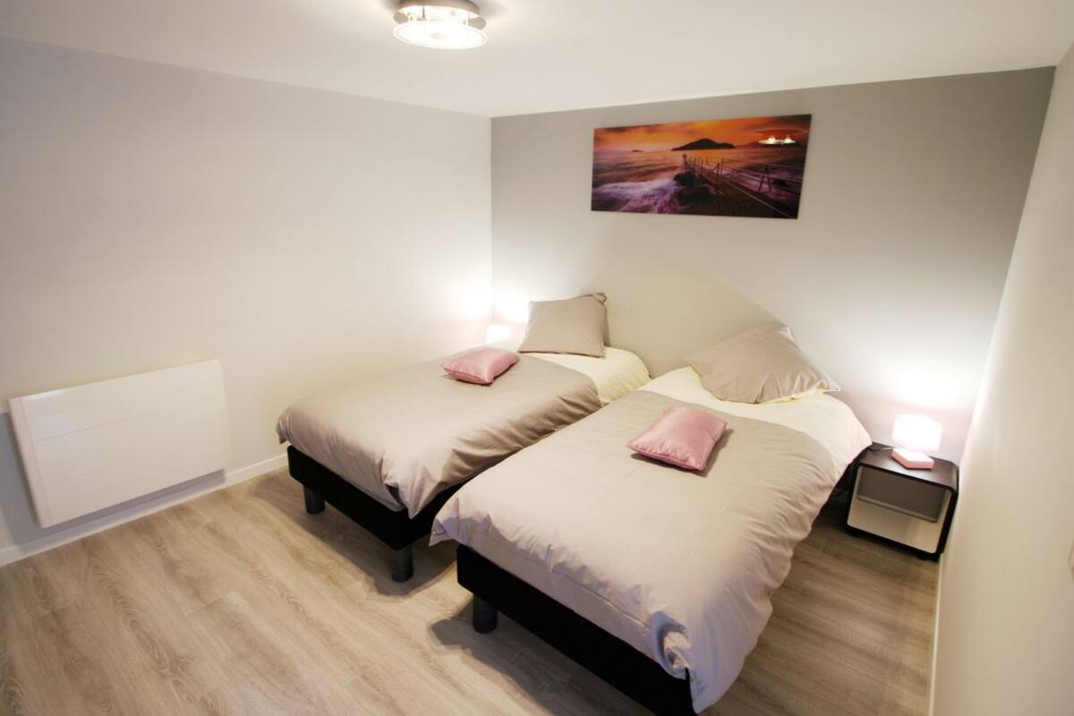 Une chambre avec deux lits, une table de chevet, un tableau accroché au mur et un luminaire au plafond.