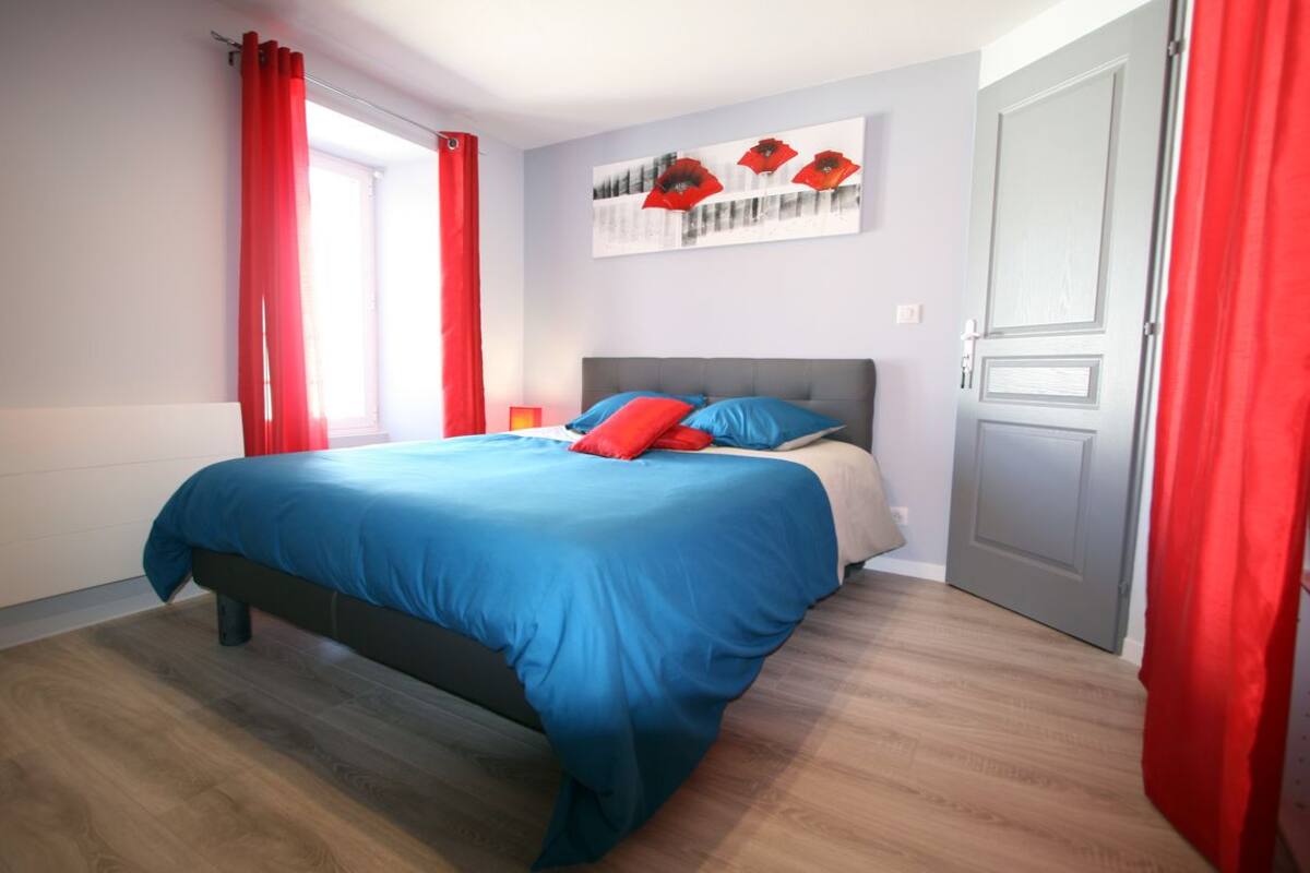 Une chambre à coucher avec un lit, des rideaux rouges, une porte grise et une fenêtre.