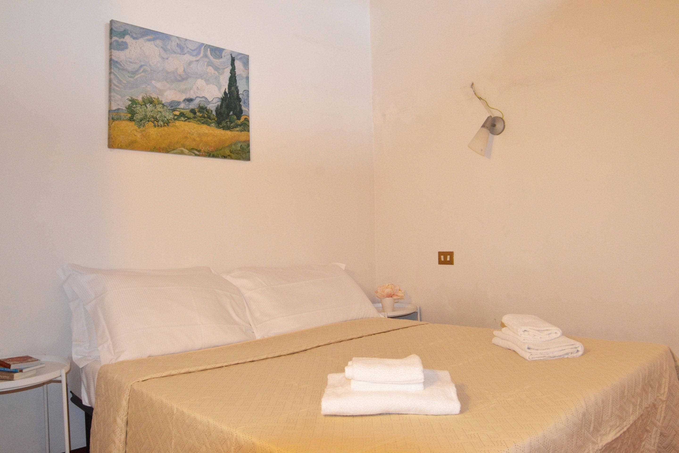A hotel room with a bed, white pillows, a beige bedspread, and a painting on the wall.