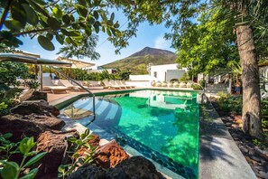 Piscina cristalina con una montaña al fondo, rodeada de sillas de descanso y rocas.