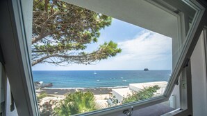 A window view of a beach with clear skies, a sandy shore, and a few boats. - Il Gabbiano Relais (Lipari)