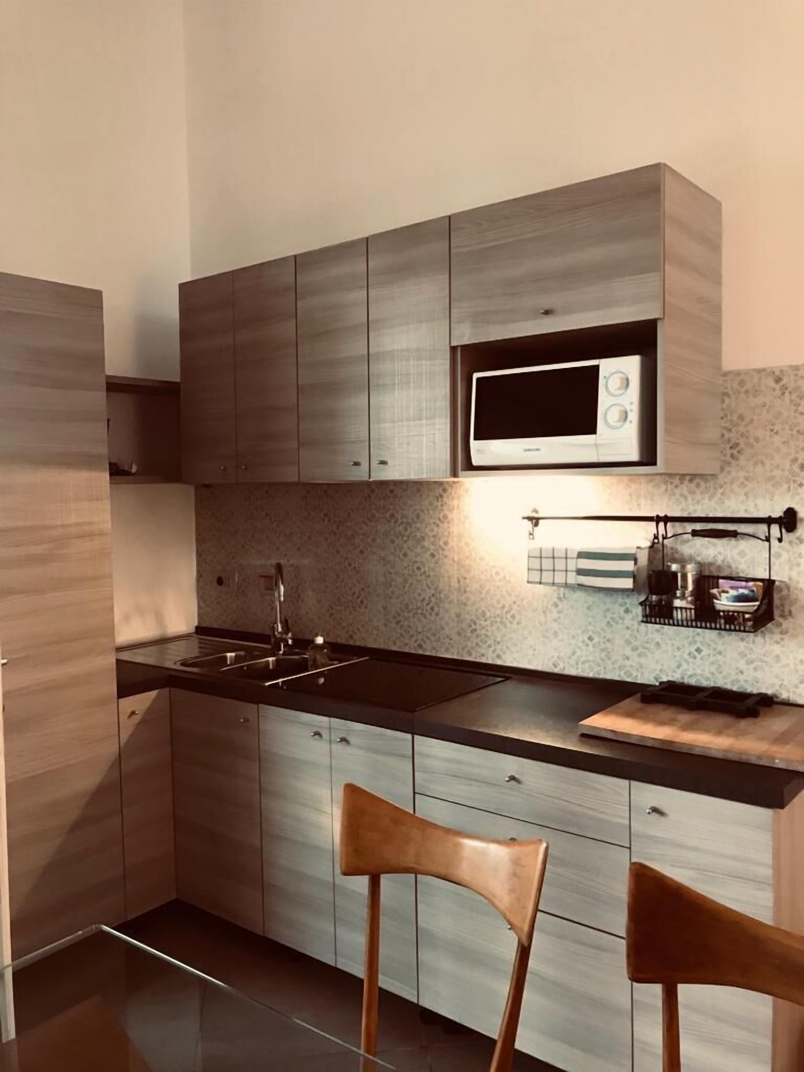 A modern kitchen with wooden cabinets, a black countertop, a microwave, and a hanging rack with kitchen utensils.