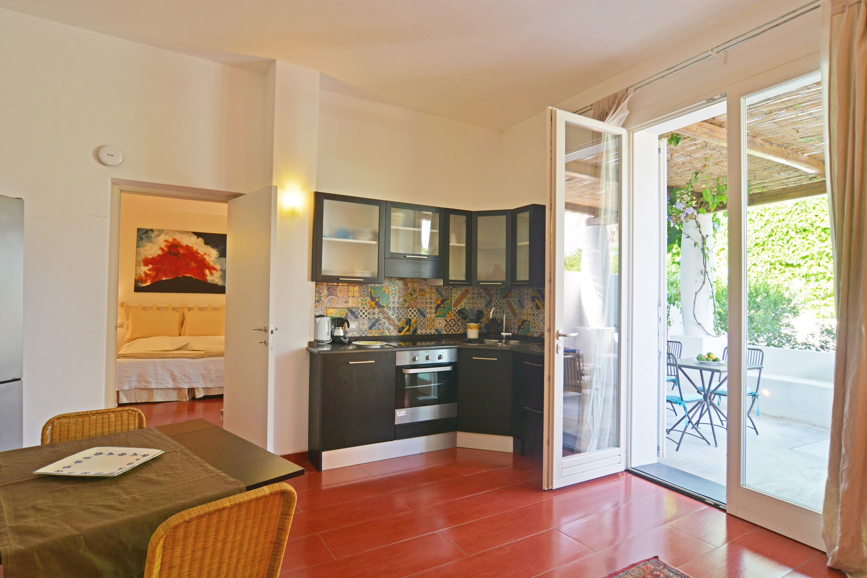 Una cocina compacta con armarios oscuros, salpicadero de azulejos y una zona de comedor con sillas de mimbre.